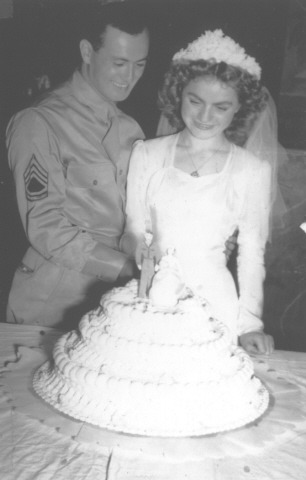 A Jewish bride and groom pose cutting their wedding cake.  Pictured are Harry Jagoda with his Yugoslavian Jewish bride, Florica Kabilio.